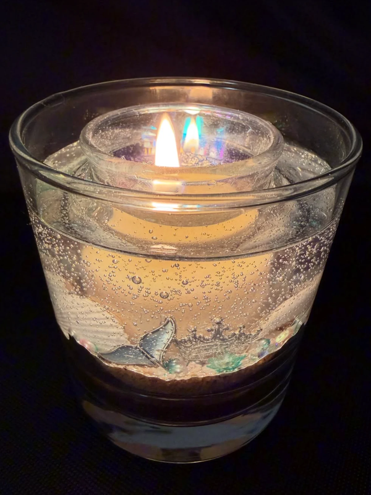 Vela luminária artesanal em vidro transparente, acesa, com composição inspirada no mar