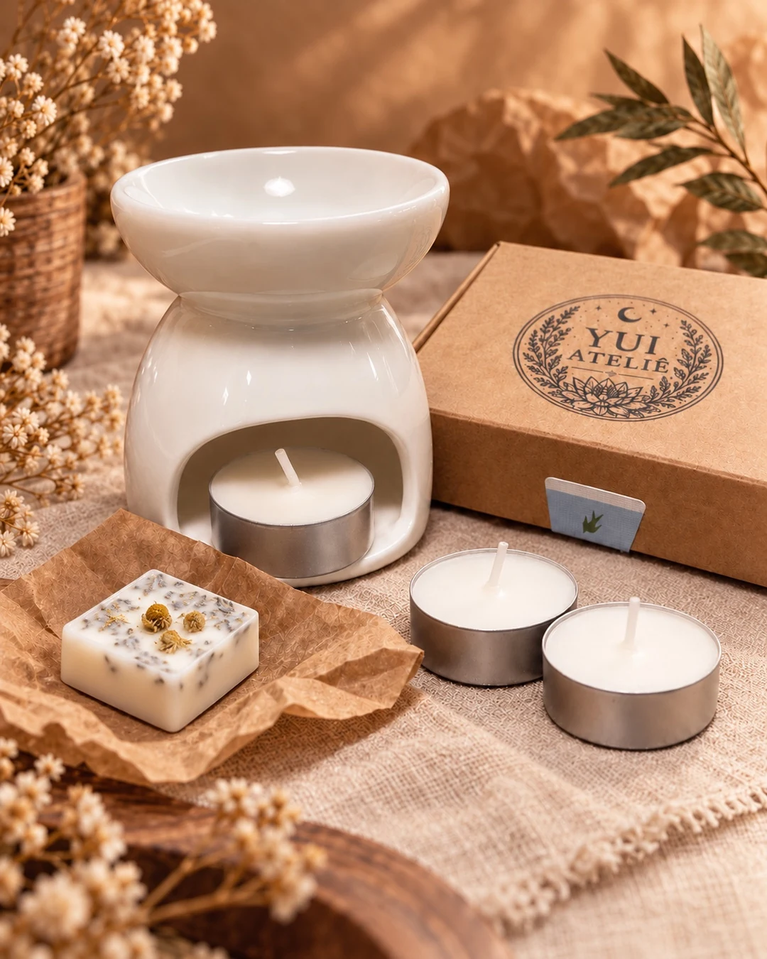 Wax Melt da Yui Ateliê ao lado de réchaud branco, velas tea light e embalagem kraft